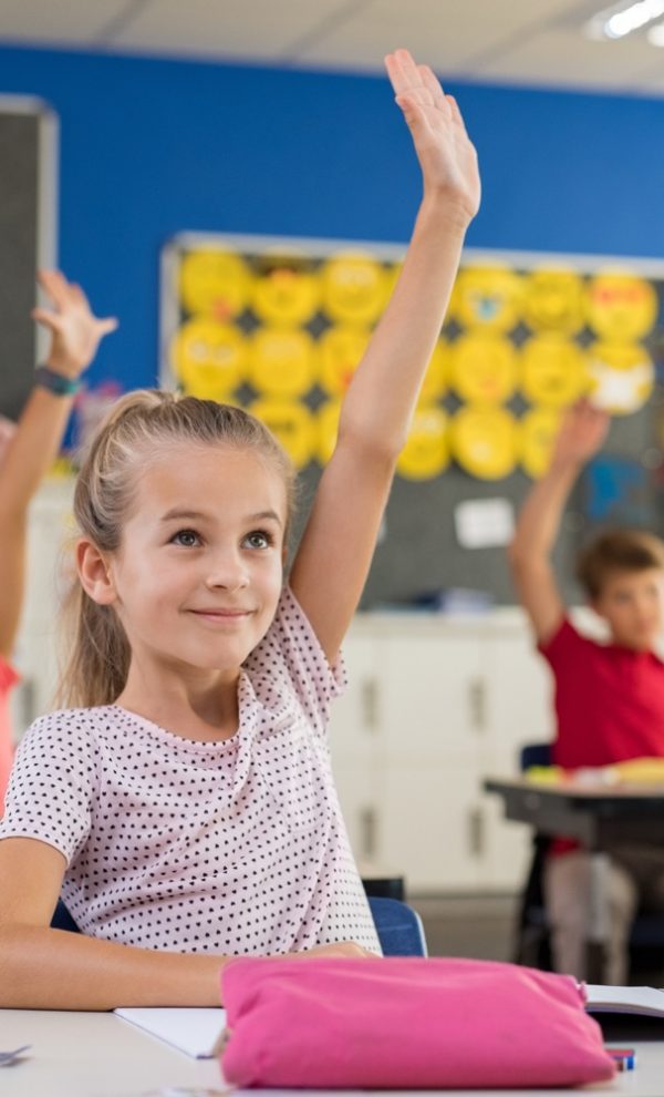 Multiethnic group of young school children raising their hands to answer a question posed by the teacher. Group of elementary kids sitting in classroom and raising hands. Clever girl raising hand knowing the answer.