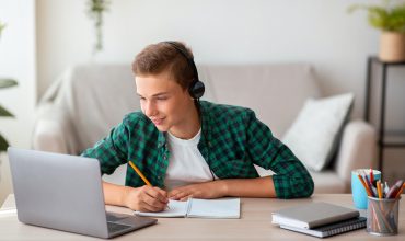 Joyful teen guy writing at notebook and looking at laptop Joyful teen guy writing at notebook and looking at laptop