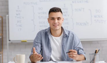 Online teacher speaking by webcam, sitting at table in home office and explaining rules english Online teacher speaking by webcam, sitting at table in home office and explaining rules english