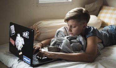 Young caucasian boy lying using computer laptop on bed Young caucasian boy lying using computer laptop on bed