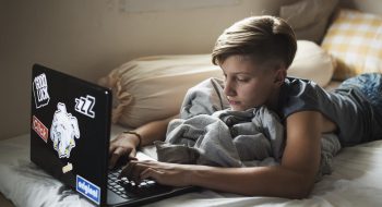 Young caucasian boy lying using computer laptop on bed